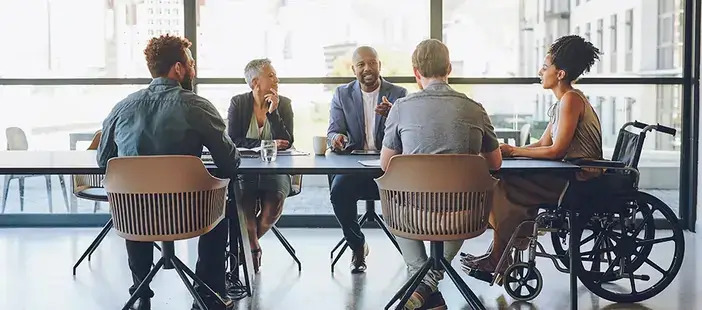 A group of individuals engaged in discussion while seated around a conference table in a meeting room.