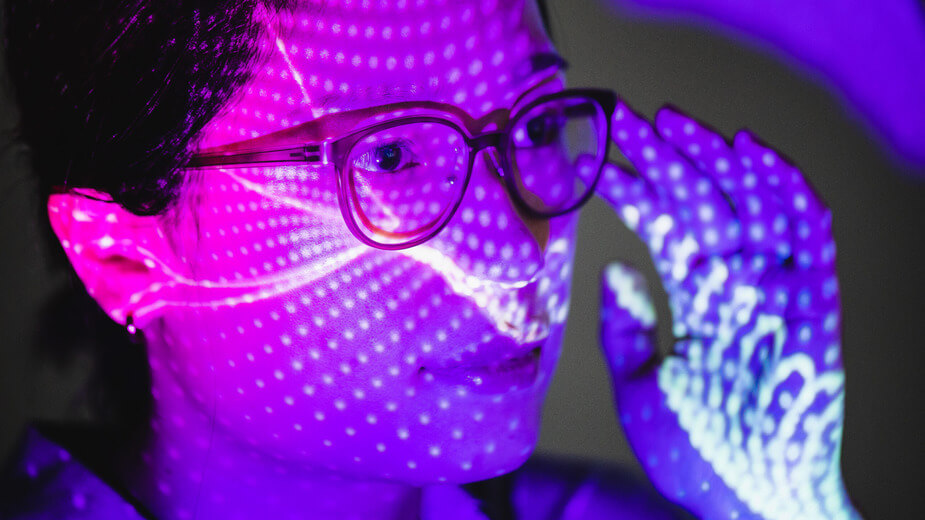 A woman with glasses illuminated by a soft purple light, creating a serene and contemplative atmosphere.