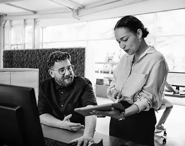 A man and woman collaborate on a computer, focused on their work in a professional setting.
