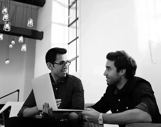 two man are talking in front of the laptop